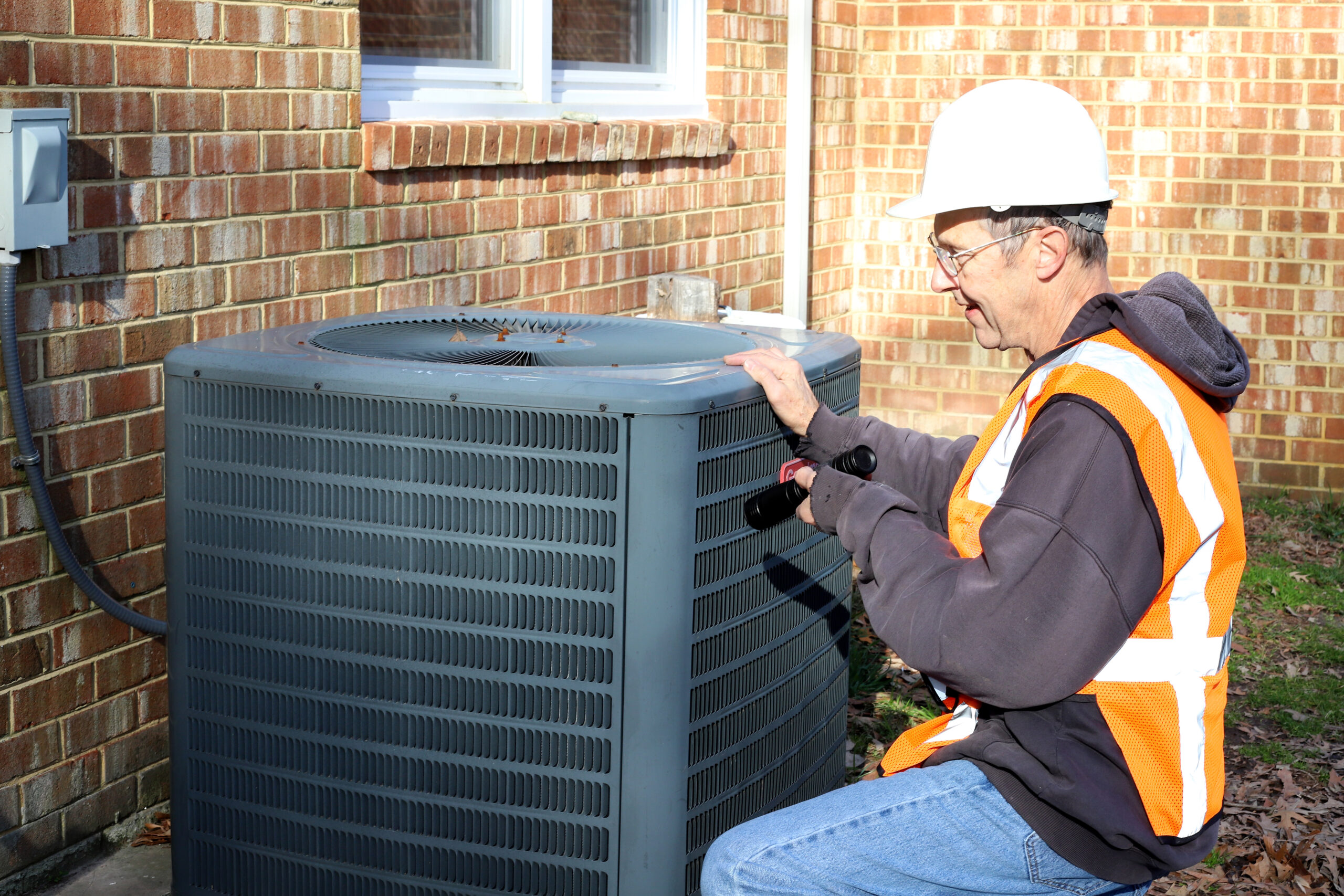 Worker inspecting outdoor air conditioning unit.